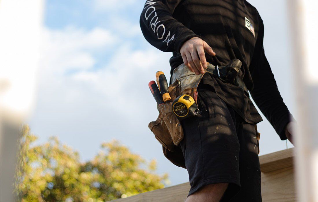 A Man is Standing on a Roof With a Tool Belt — MoneySmith Group In Kingscliff, NSW
