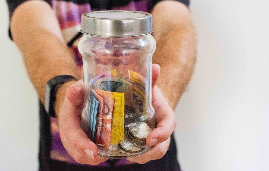 A Man is Holding a Jar Filled With Money — MoneySmith Group In Kingscliff, NSW