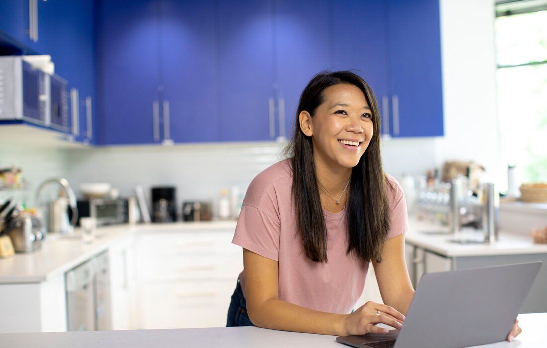 Woman is Sitting at a Kitchen Counter Using a Laptop Computer — MoneySmith Group In Kingscliff, NSW