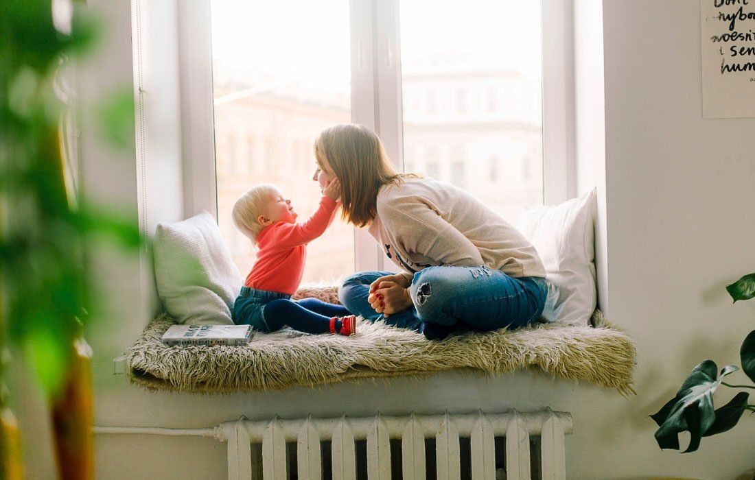A Woman is Sitting on a Window With a Baby — MoneySmith Group In Kingscliff, NSW