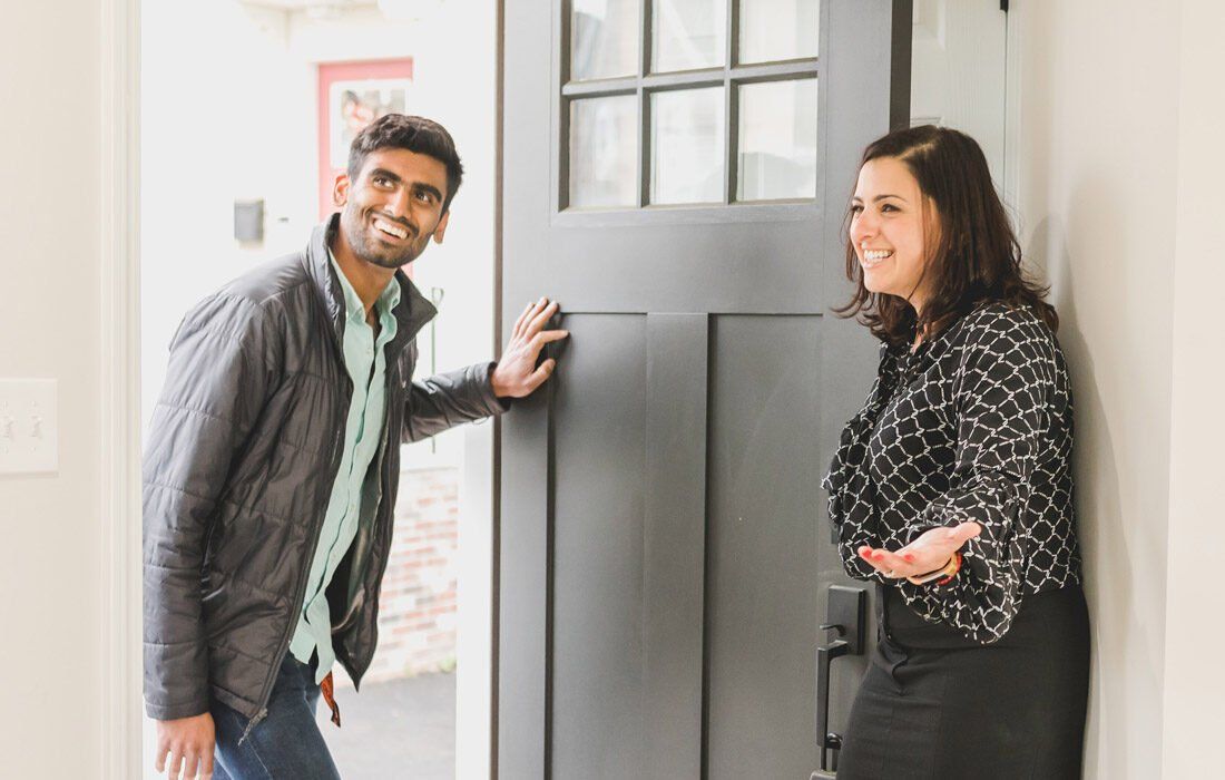 A person in a gray jacket smiles as they enter a home through a dark gray door — MoneySmith Group In Kingscliff, NSW