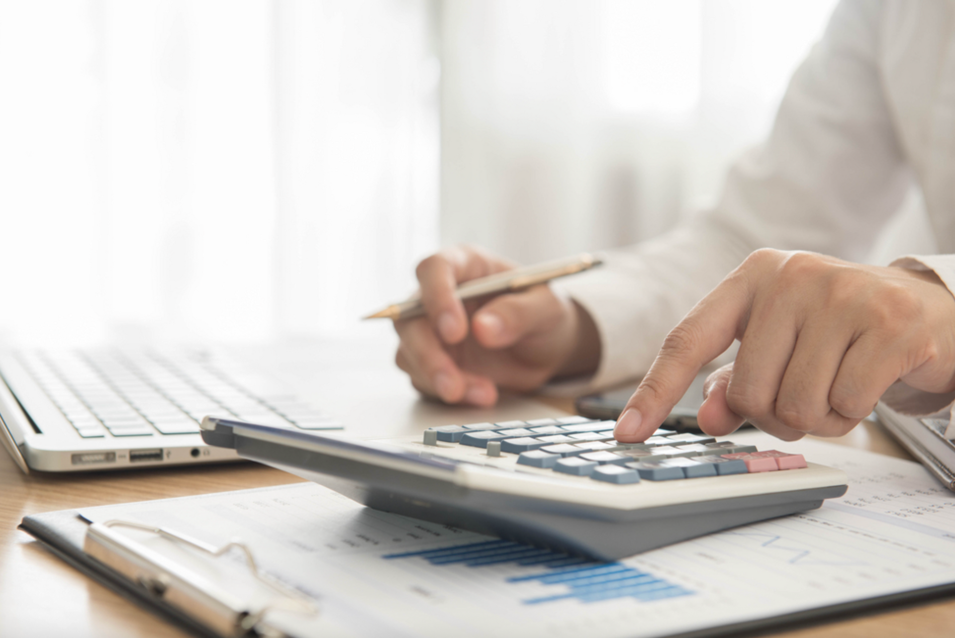 Someone sitting at a desk with a laptop and calculator and paperwork. 