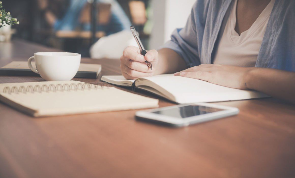 A Woman is Sitting at a Table Writing — MoneySmith Group In Kingscliff, NSW