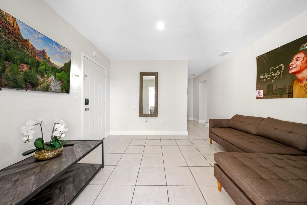 A modern, light-filled living room featuring tile floors, a brown sectional sofa, a coffee table, and wall art.
