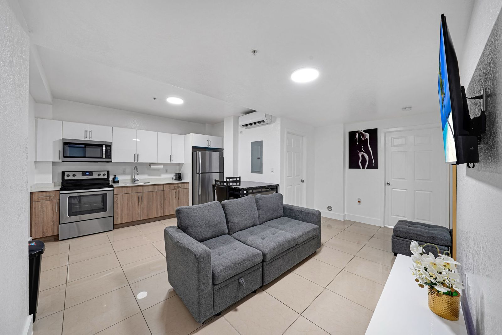 Modern apartment with a grey sofa, kitchen area, stainless steel appliances, and tile flooring.