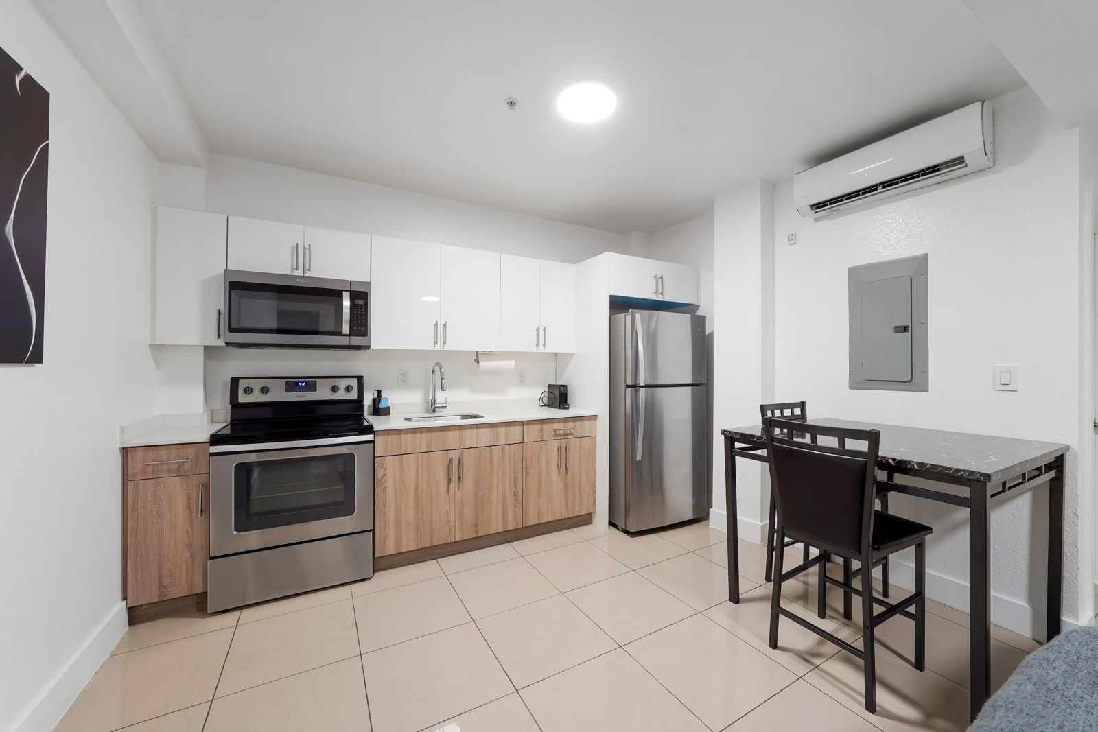 A modern kitchen with light wood lower cabinets, white upper cabinets, stainless steel appliances, and a dining table.