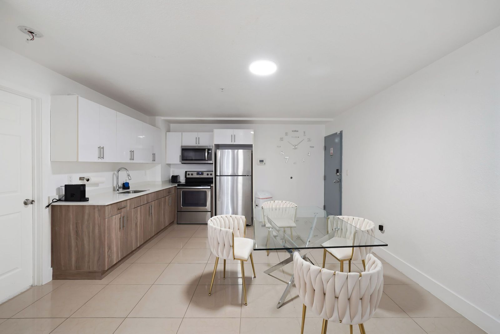 A modern, open-concept kitchen and dining area with white cabinets, wood-tone lower cabinets, and a glass dining table.