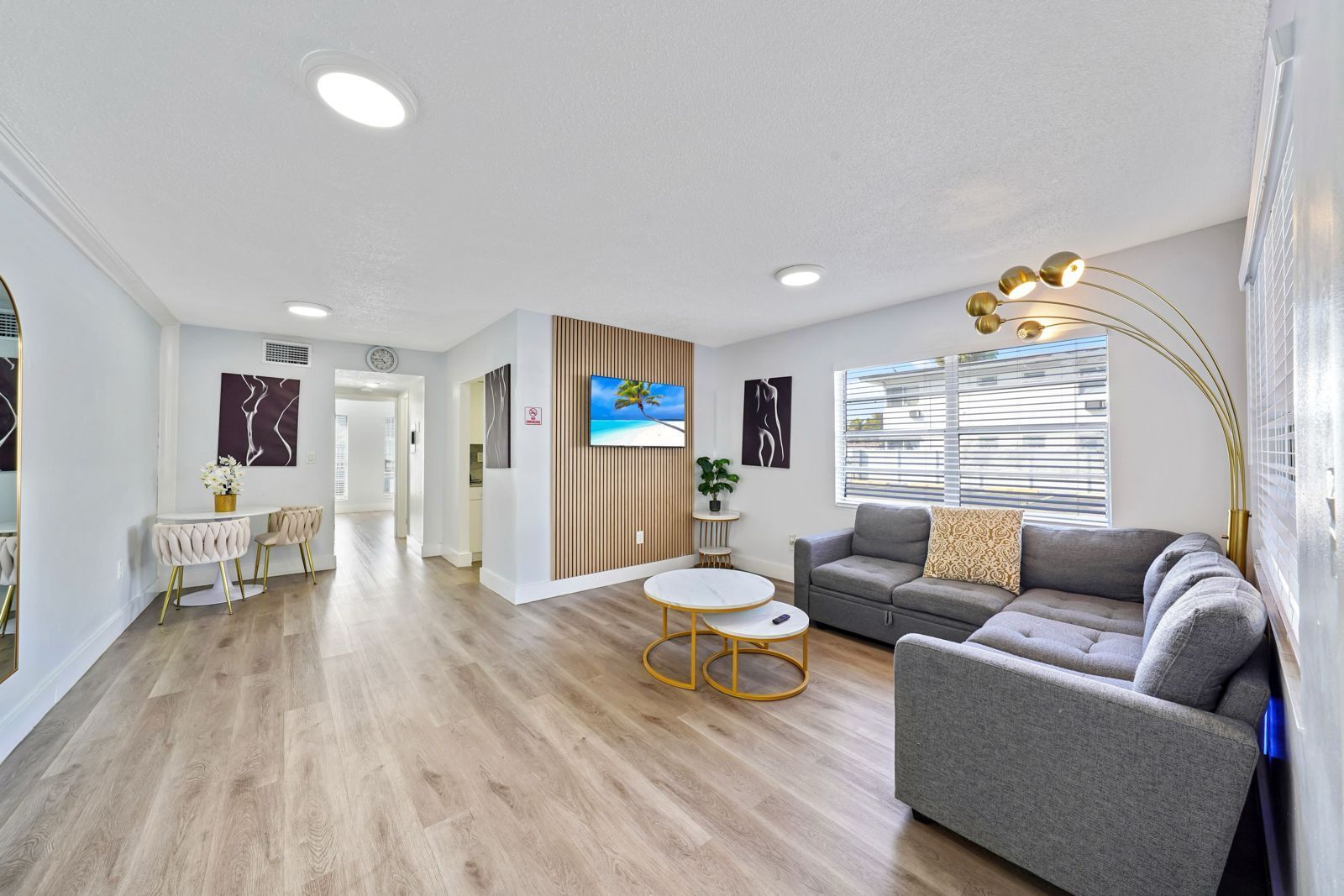 A modern living room with light wood floors, a grey sectional sofa, nesting coffee tables, and a wall-mounted TV.