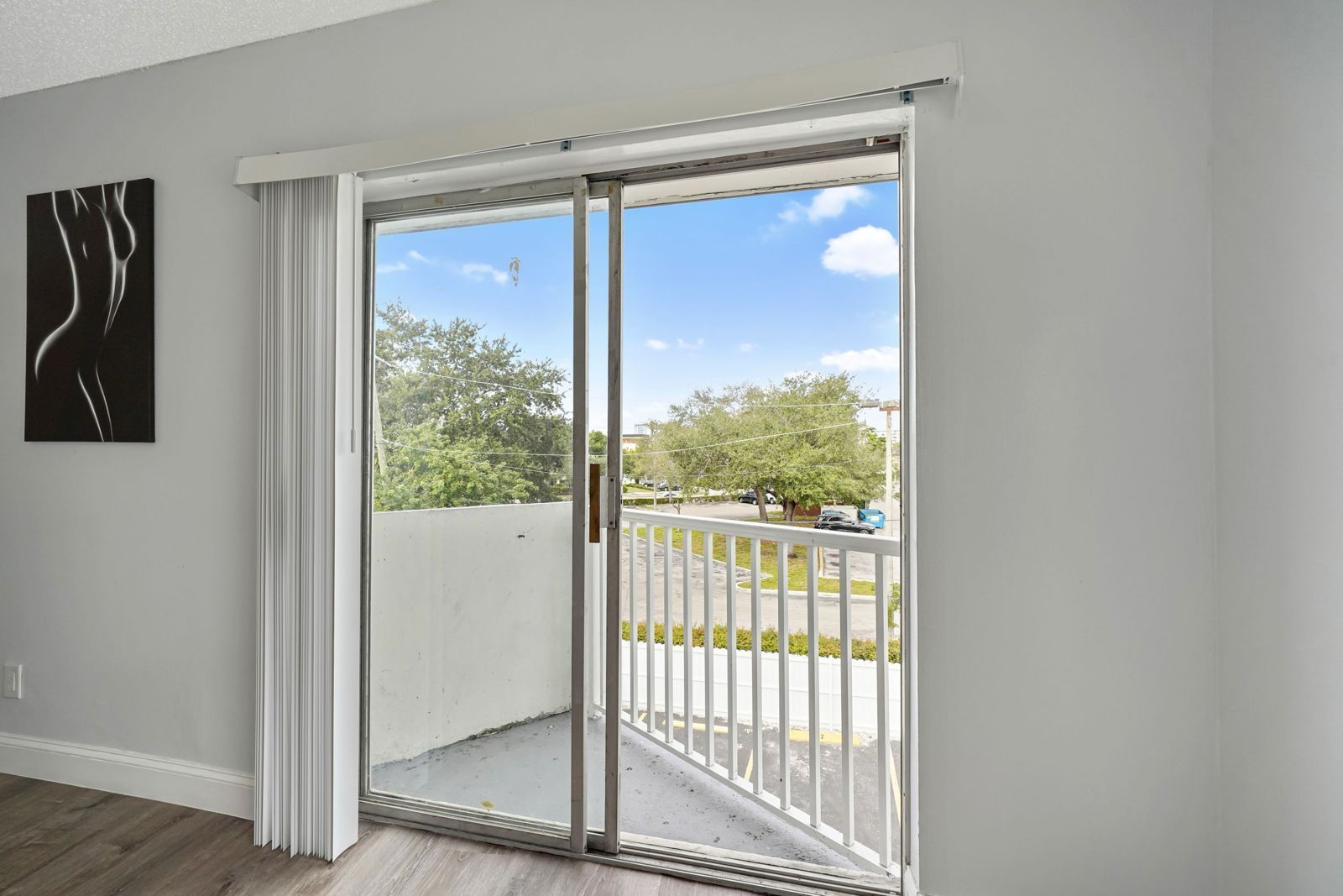 A sliding glass door opens to a balcony overlooking trees and a parking lot, with a minimalist abstract art piece nearby.