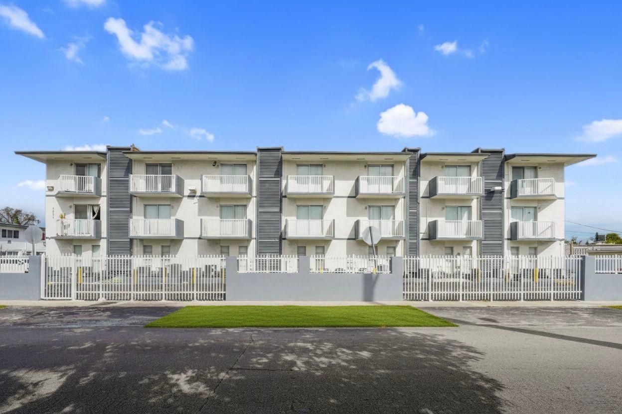 A three-story apartment building with a white facade and dark grey accents, featuring private balconies under a blue sky.