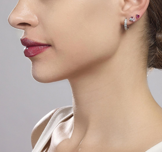 Donna che indossa orecchini di diamanti: un paio a bottone, uno pendente.