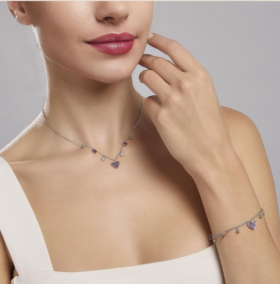 Donna con collana e braccialetto d'oro con pendenti a forma di cuore; top marrone.