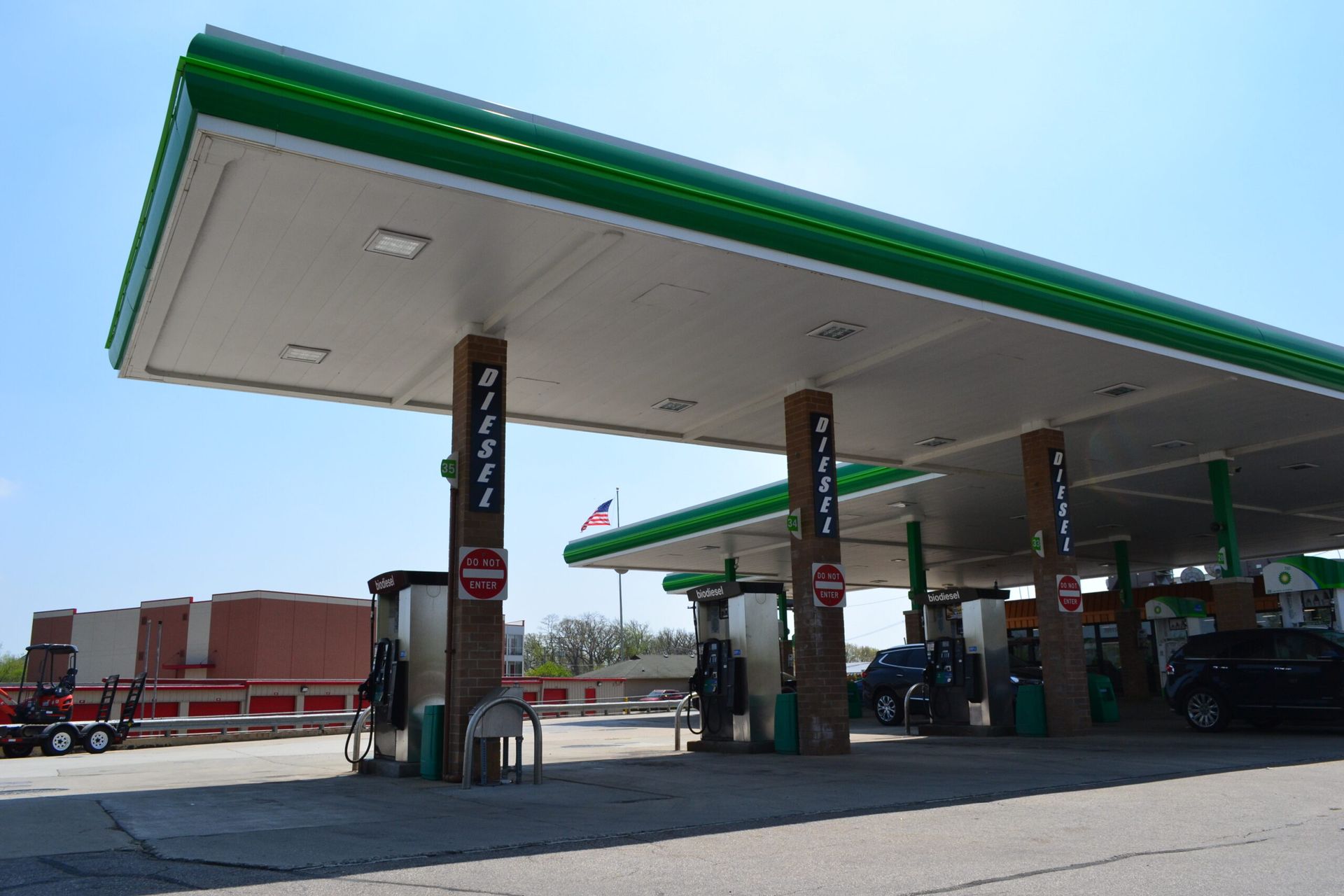 A gas station with a green roof and a brick building in the background.