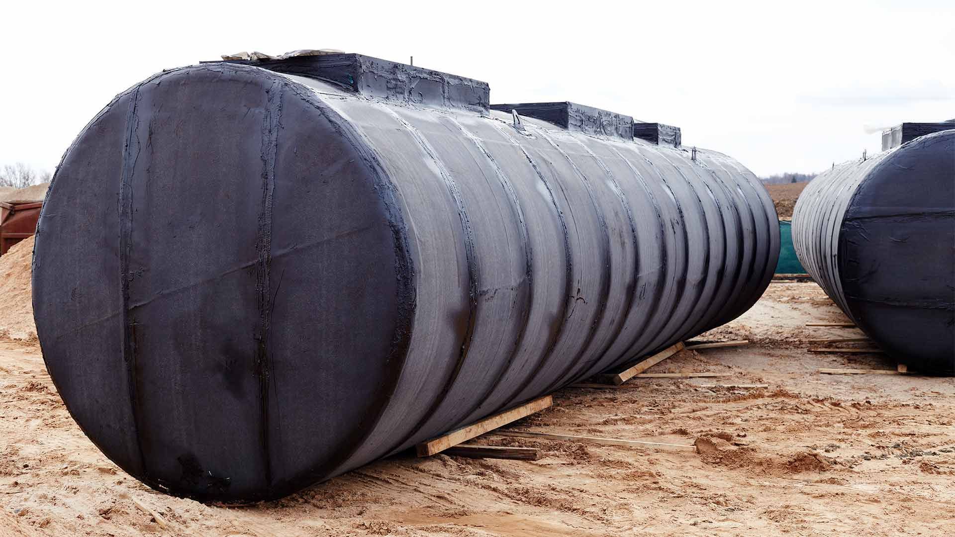 Three large black barrels are sitting in the dirt.
