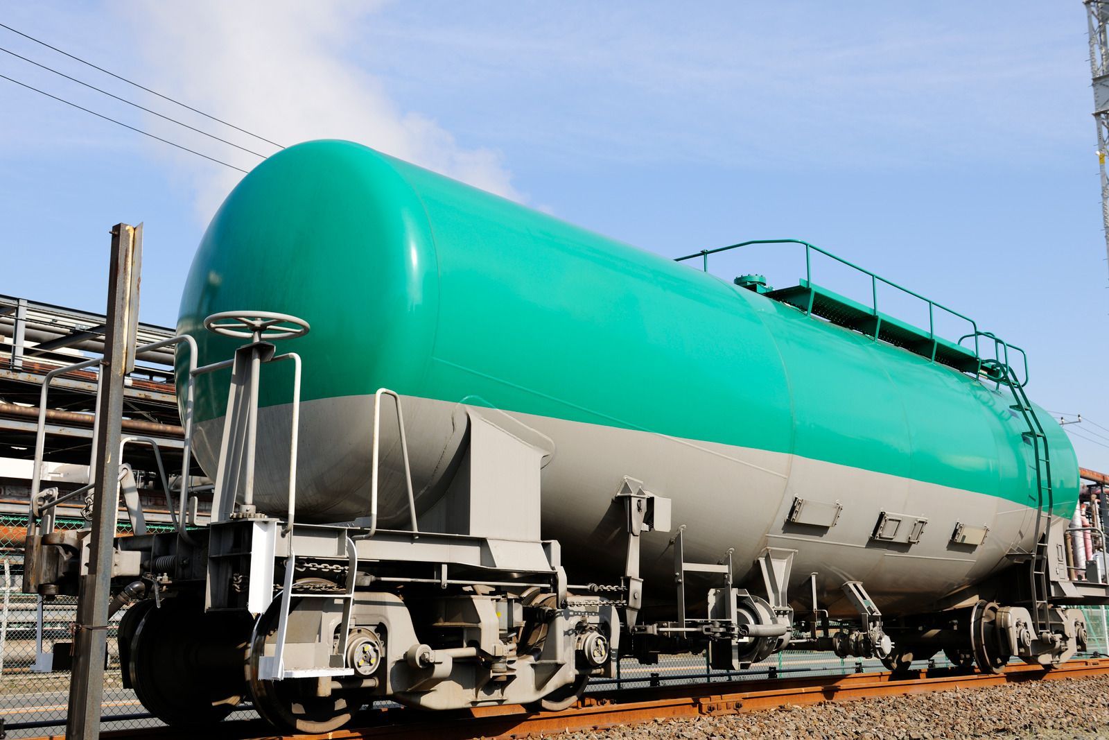 A green and gray tanker train is parked on the tracks.