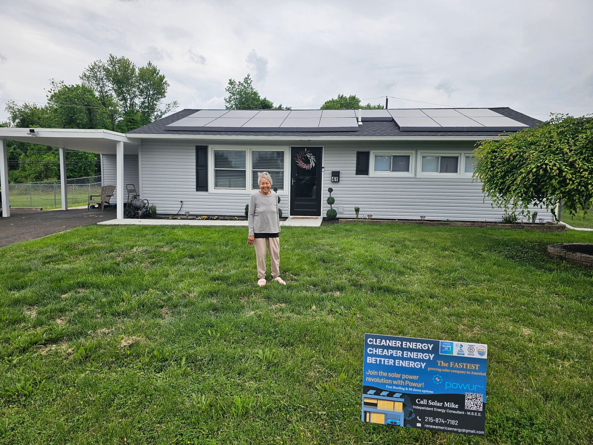 A woman is standing in front of a house with solar panels on the roof.