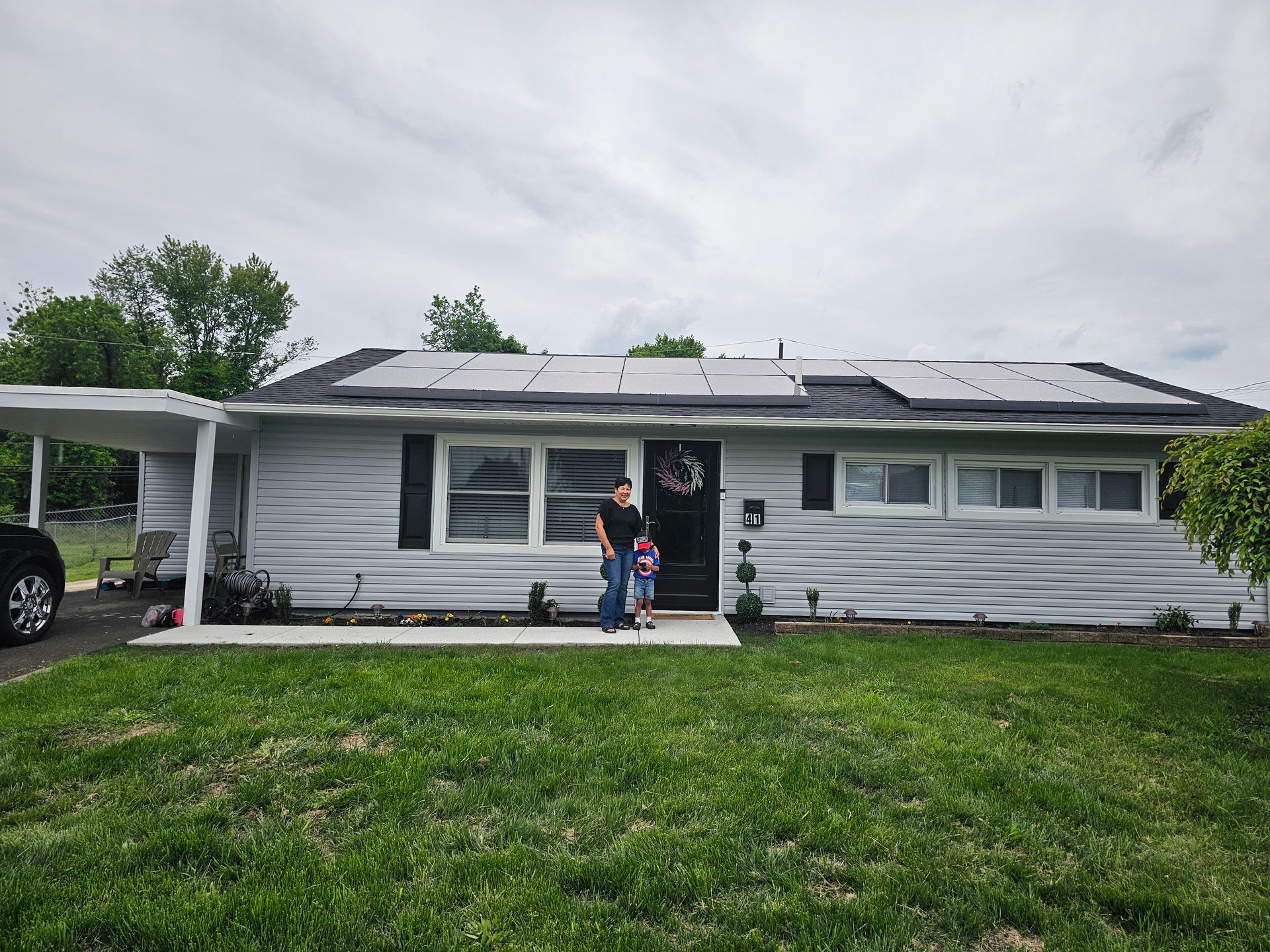 A man and a child are standing in front of a house with solar panels on the roof.