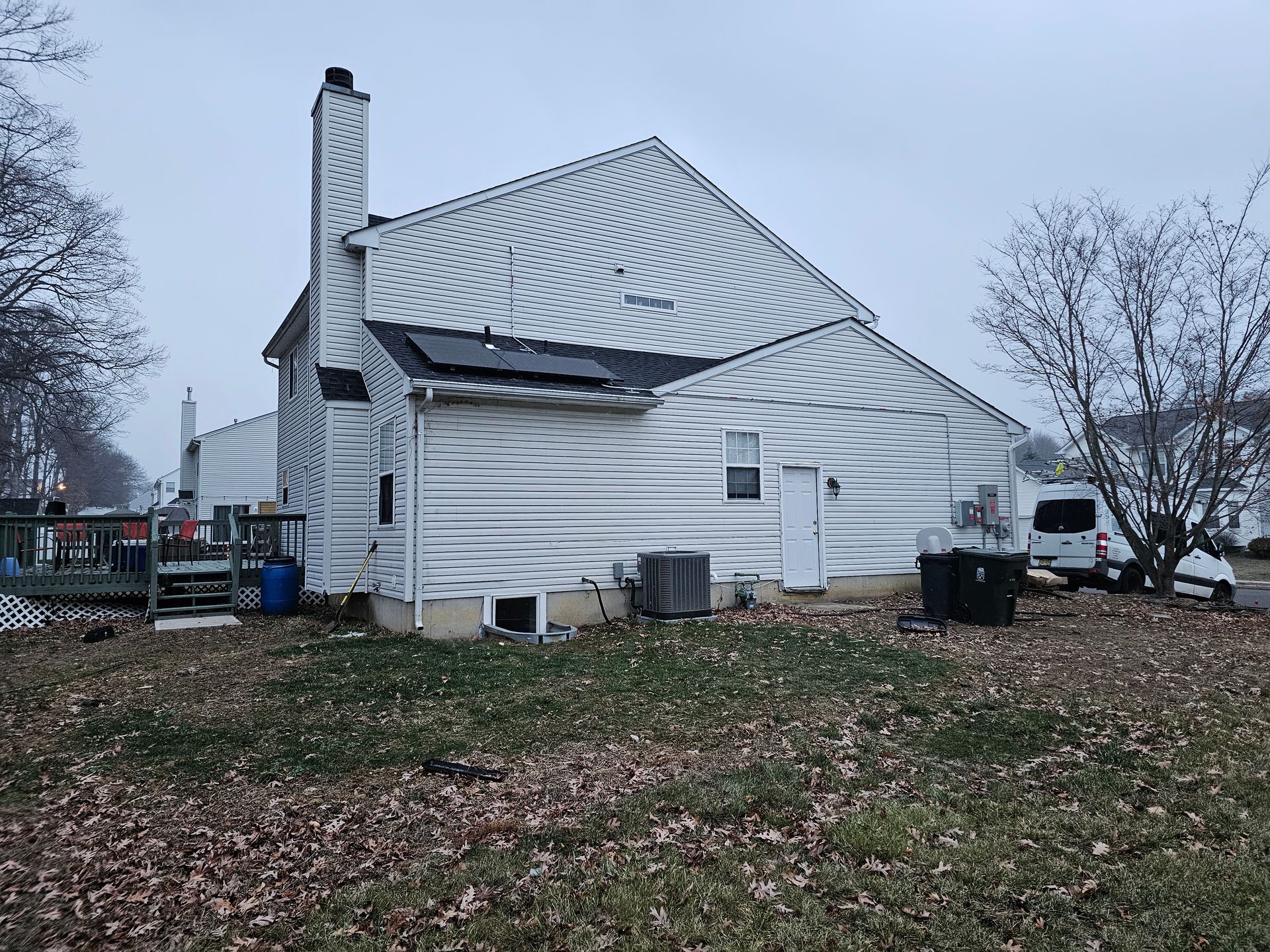 The back of a white house with a chimney and a lot of leaves on the ground.