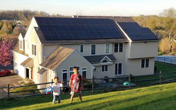 Two children are walking in front of a house with solar panels on the roof.