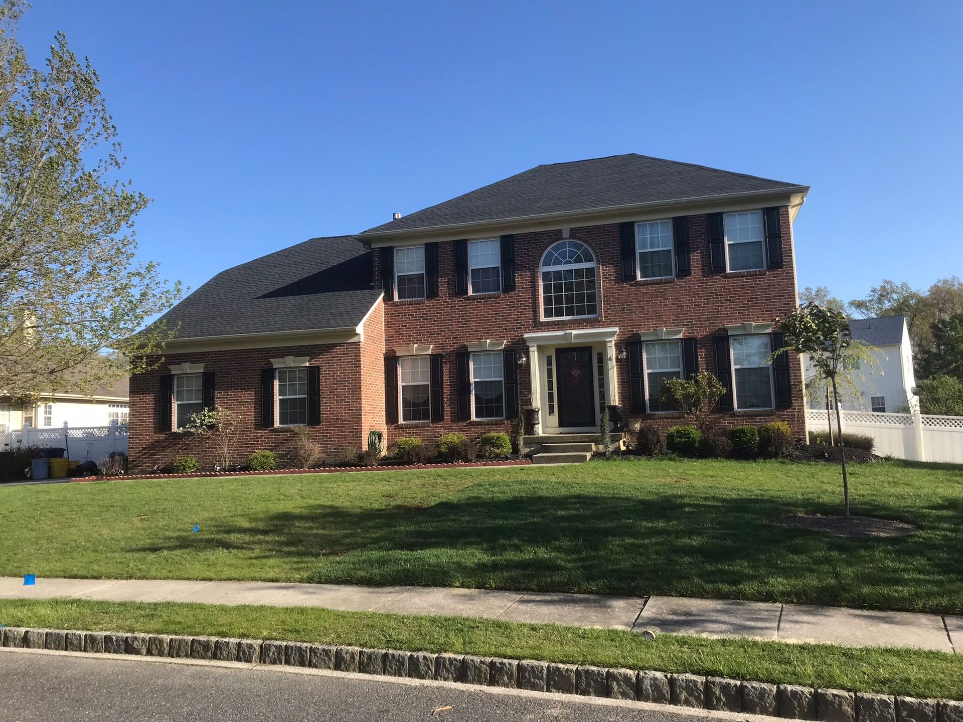 A large brick house with black shutters and a lush green lawn.