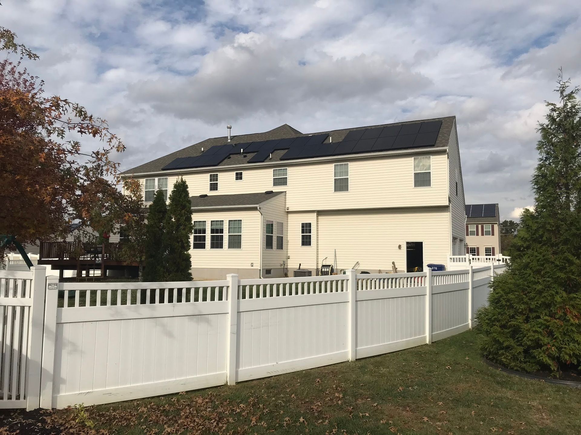 A white fence surrounds a house with solar panels on the roof