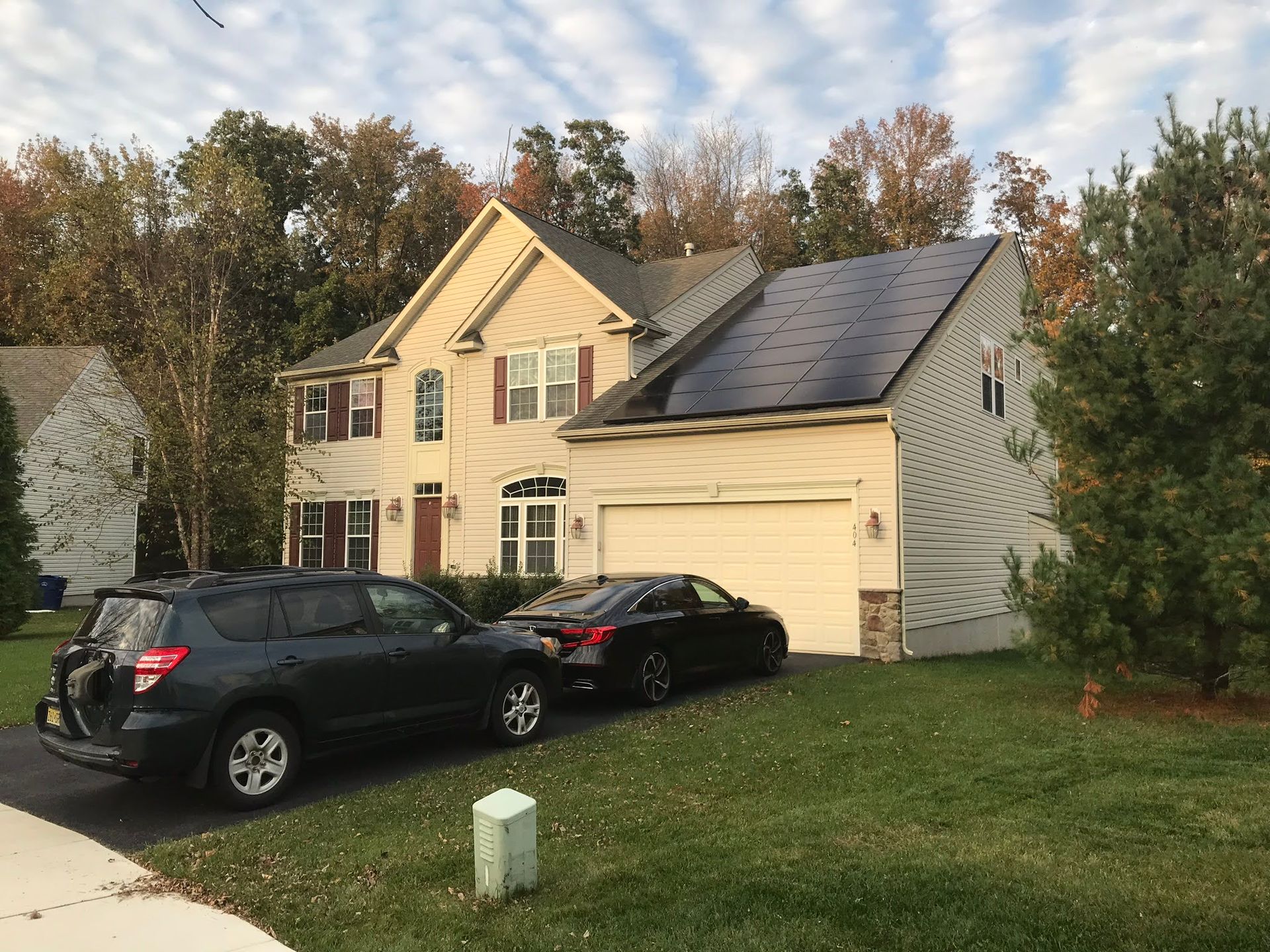 Two cars are parked in front of a house with solar panels on the roof.