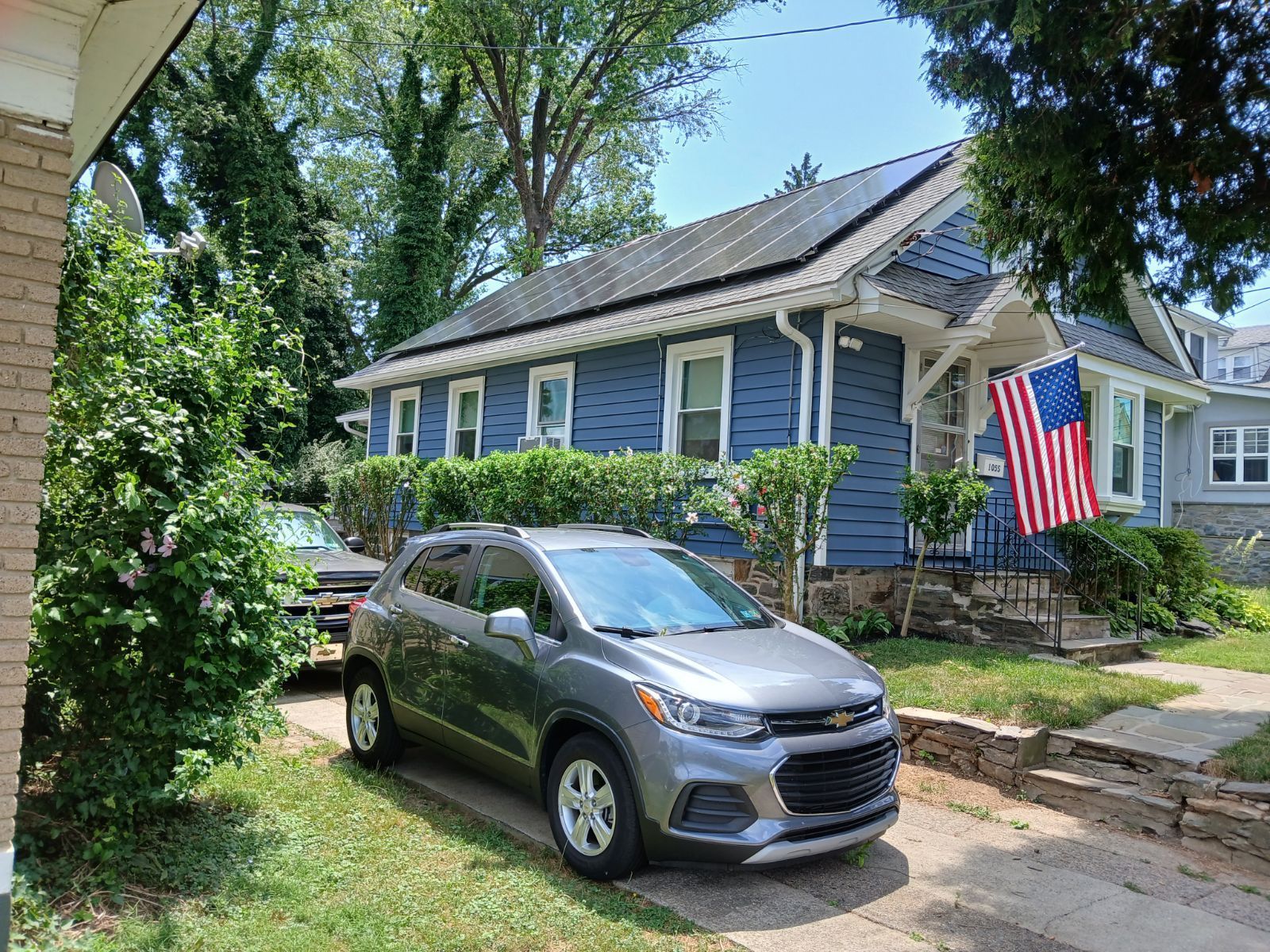 A car is parked in front of a house with solar panels on the roof.