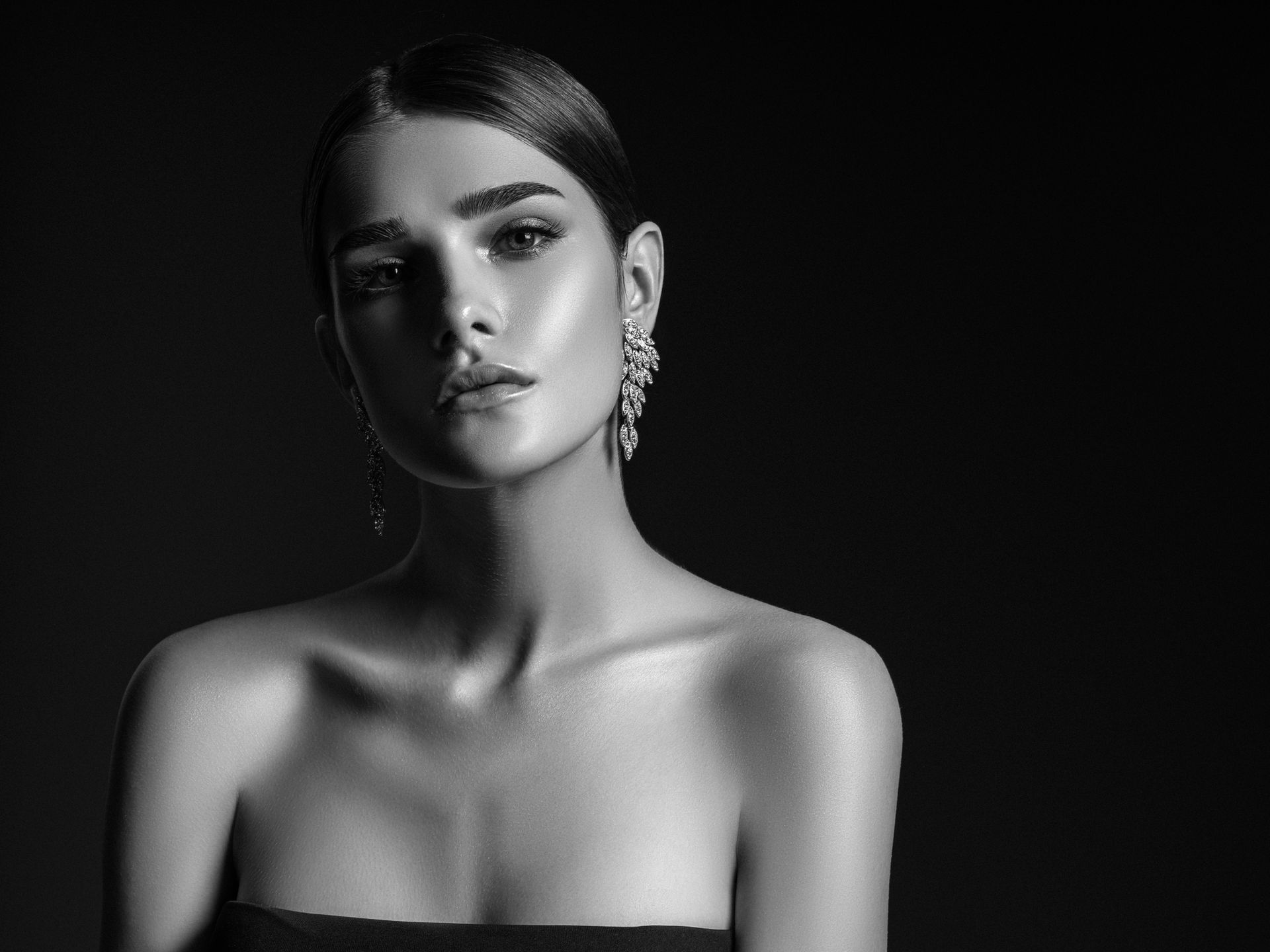 Donna con capelli scuri, orecchini e abito senza spalline, in posa su uno sfondo scuro.