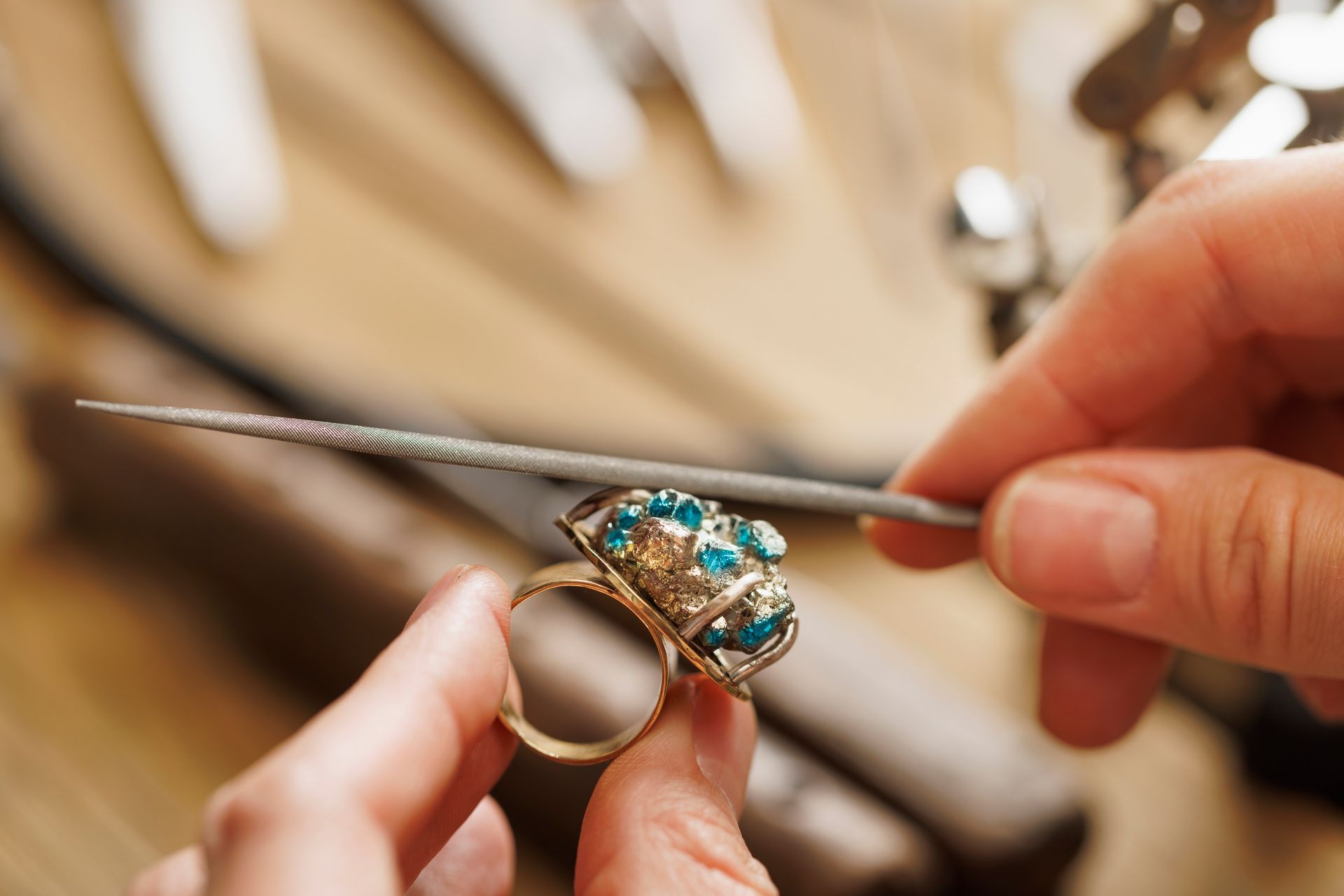 Mani di un gioielliere che lavorano su un ciondolo d'argento, utilizzando uno strumento su un blocco di legno.