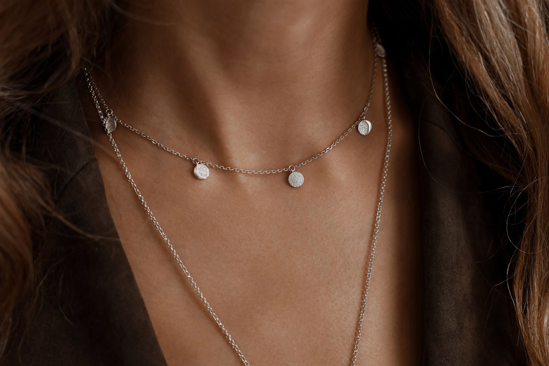 Donna che indossa due delicate collane d'argento con piccoli diamanti rotondi.
