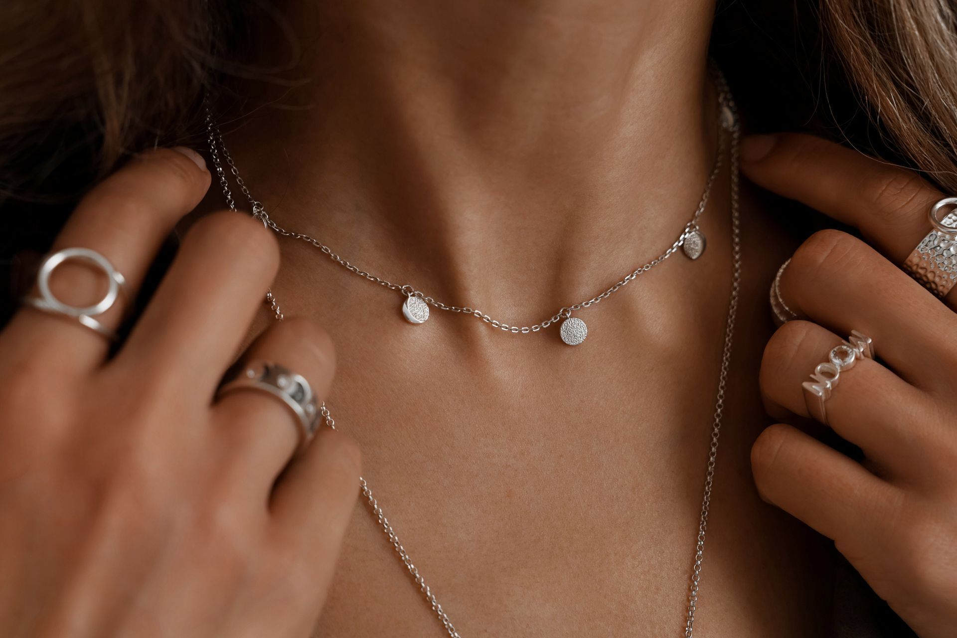 Donna che indossa diversi anelli d'argento e una delicata collana con ciondoli pendenti.