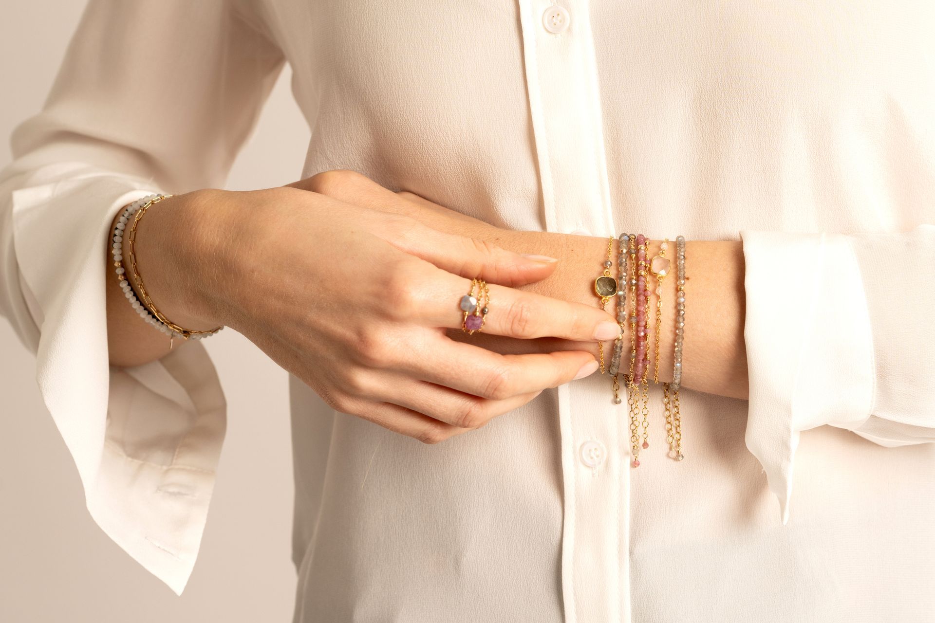 Mani di donna con anelli e braccialetti d'oro, indossati sui polsi sopra una camicia bianca abbottonata.
