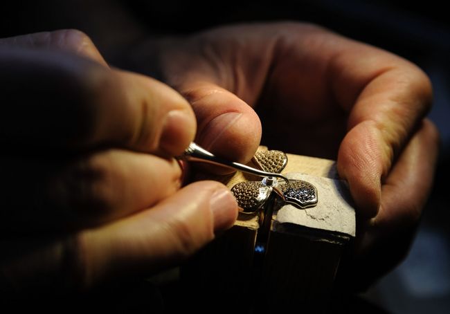 Un orologiaio usa le pinzette per assemblare un componente d'oro di un orologio, primo piano di piccoli ingranaggi e gioielli.
