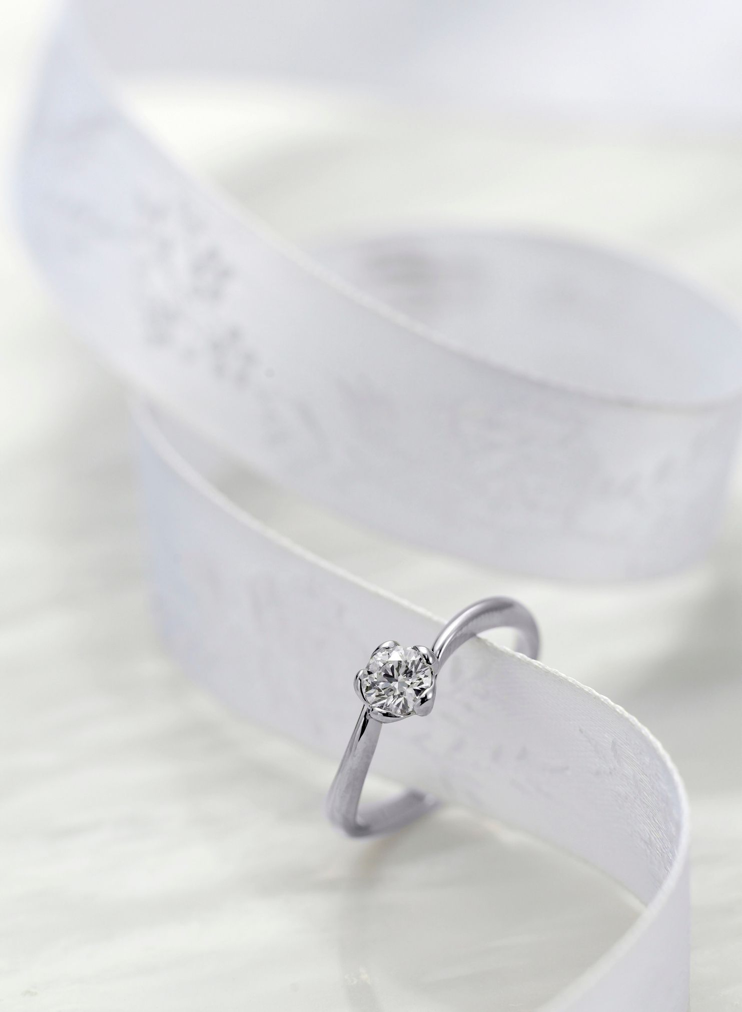 Anello con diamante su nastro bianco con bordo decorato.