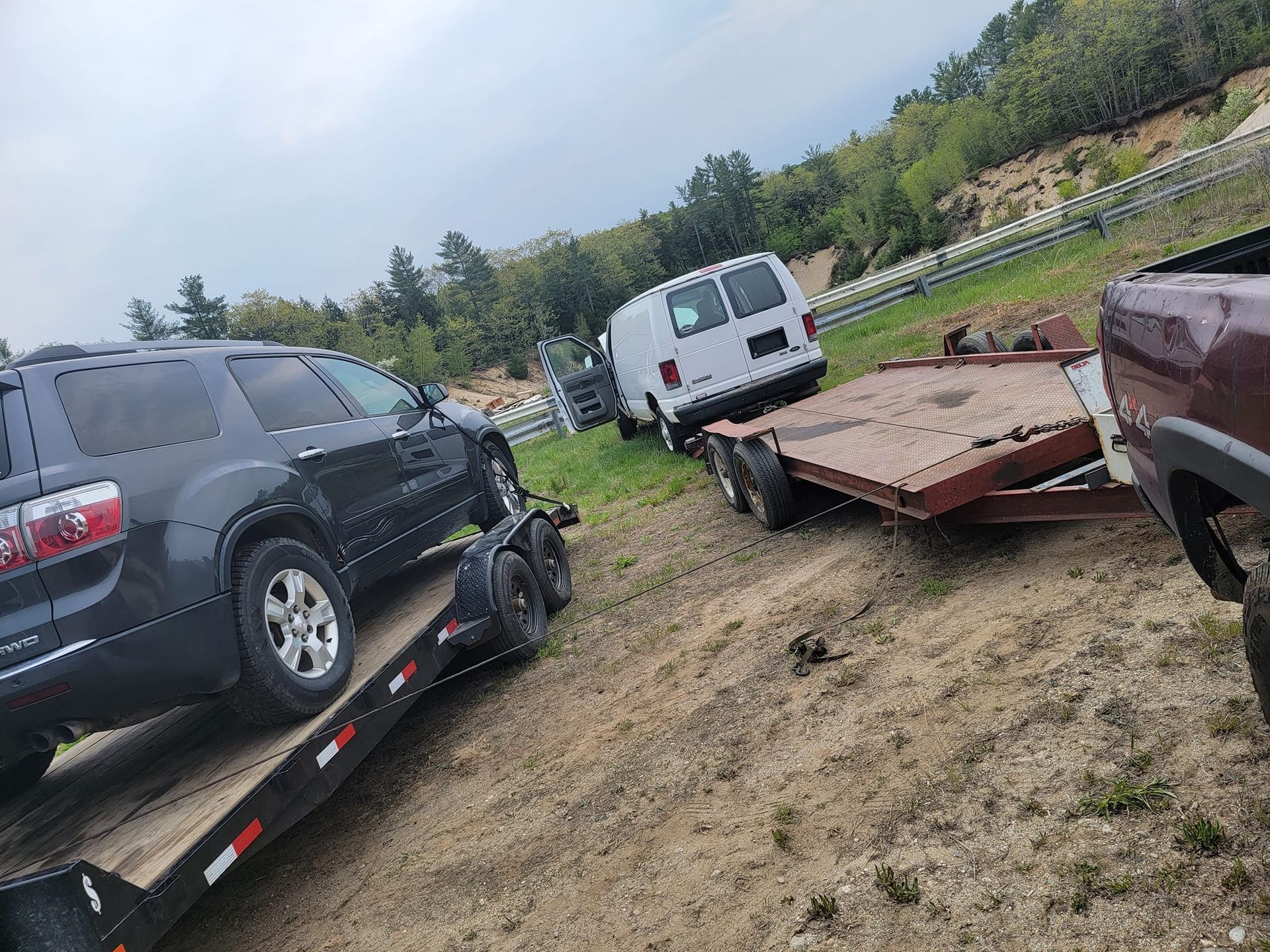 A black suv is sitting on top of a trailer next to a white van.