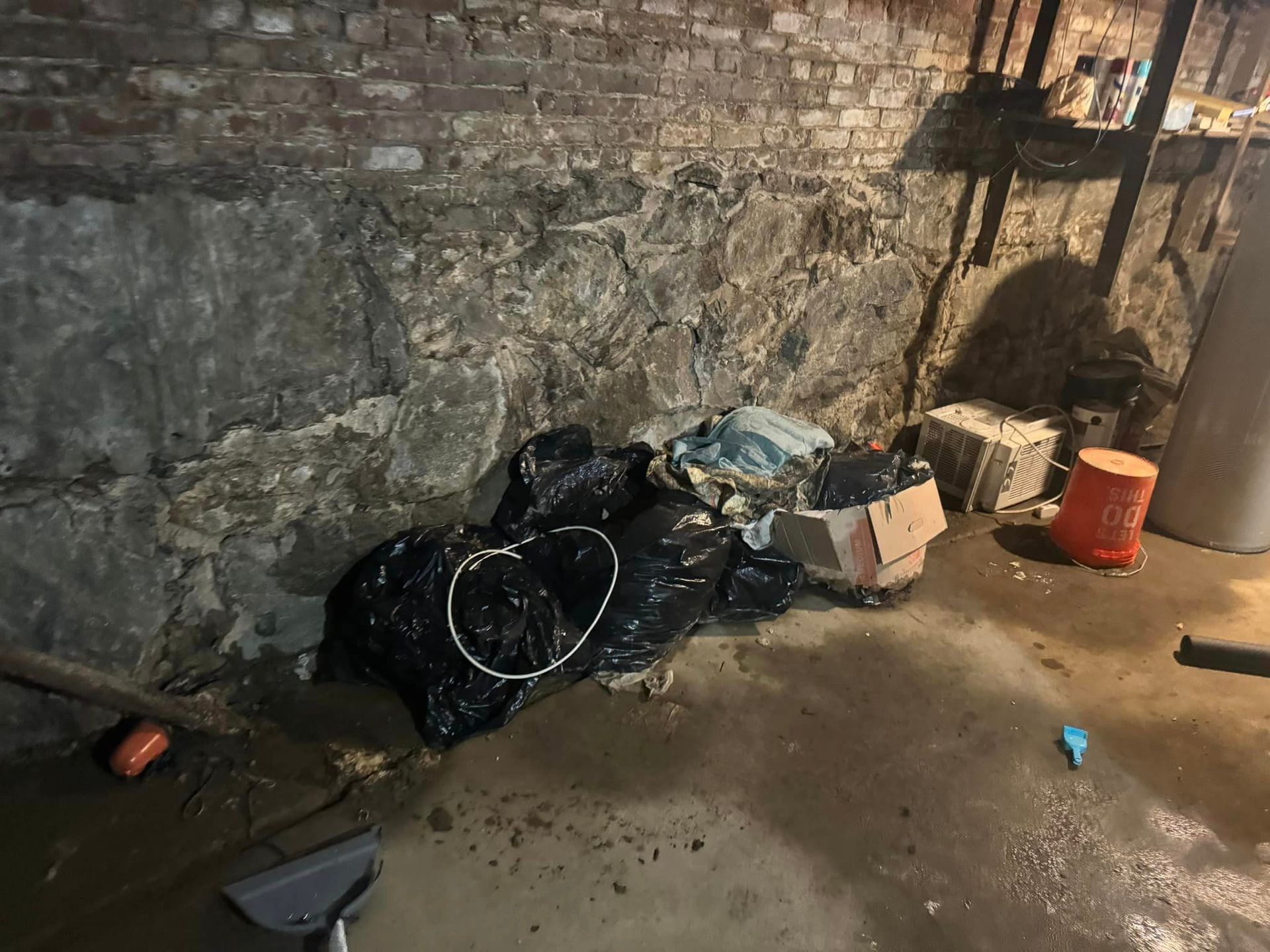 A pile of trash is sitting in a basement next to a brick wall.
