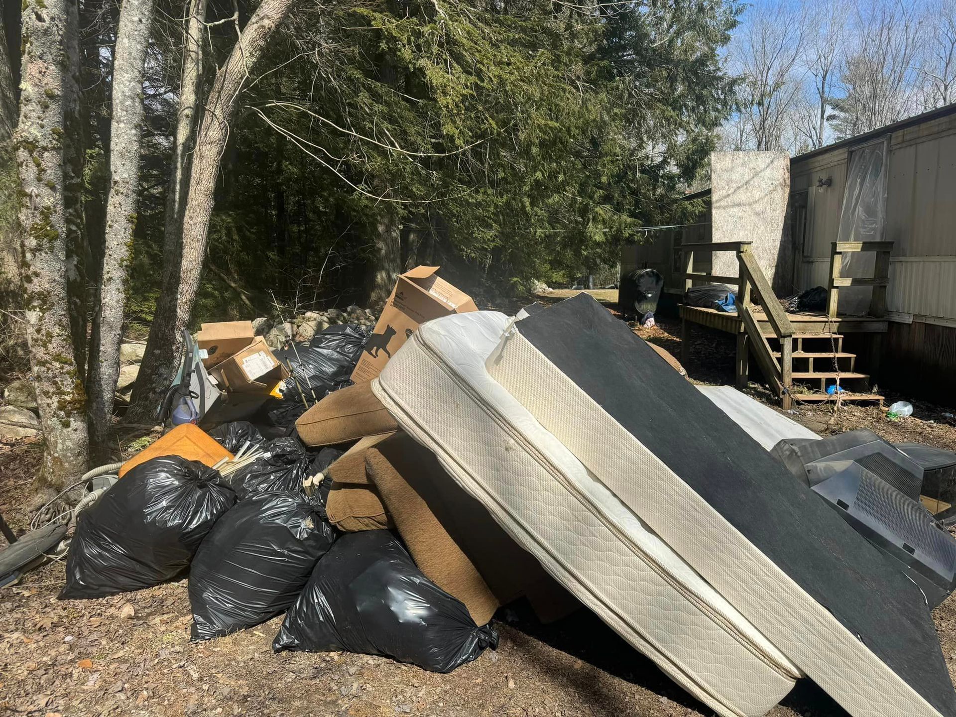 A pile of trash in a yard with a mattress on top of it.