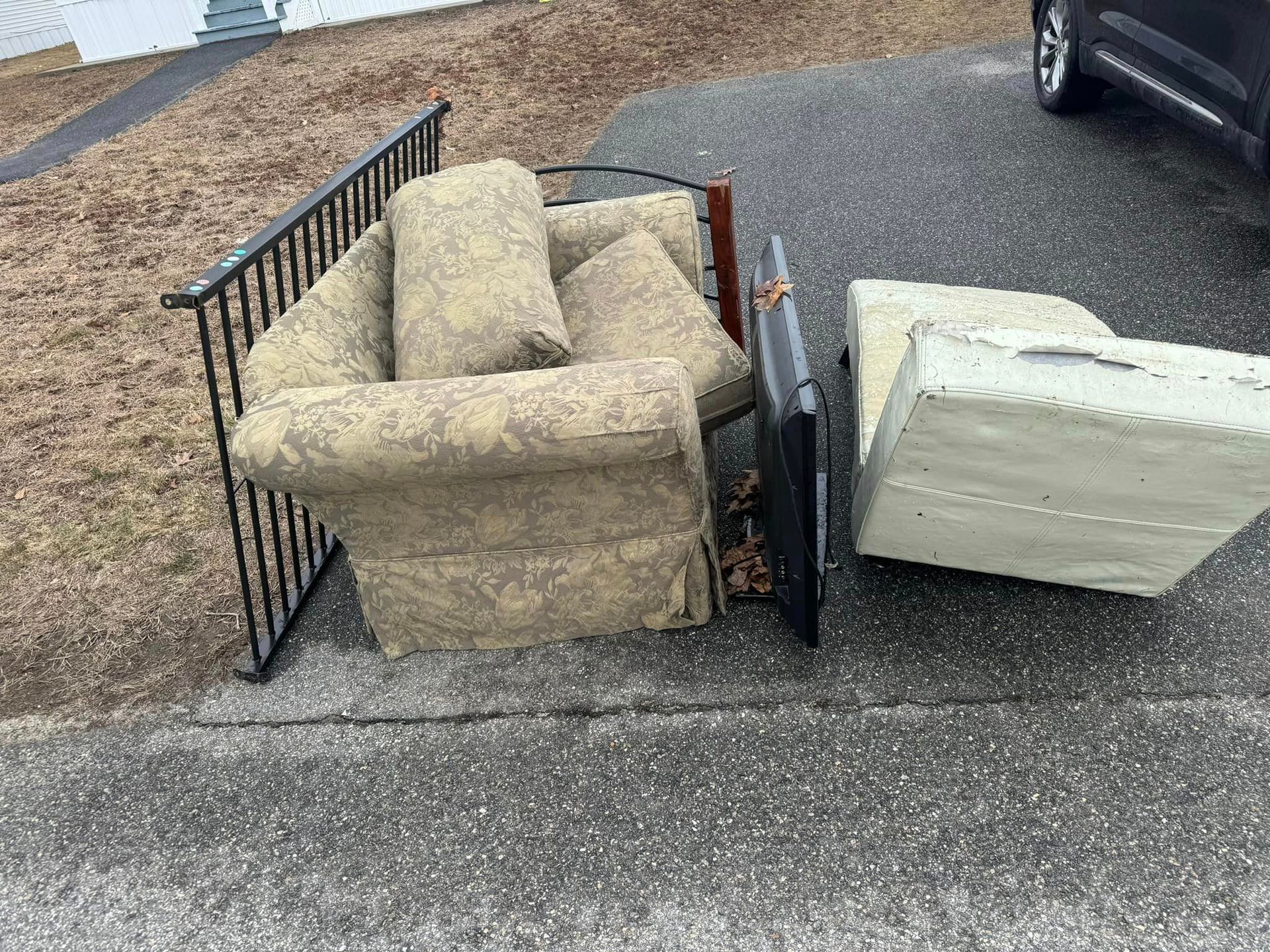 A chair and a mattress are sitting on the side of the road.