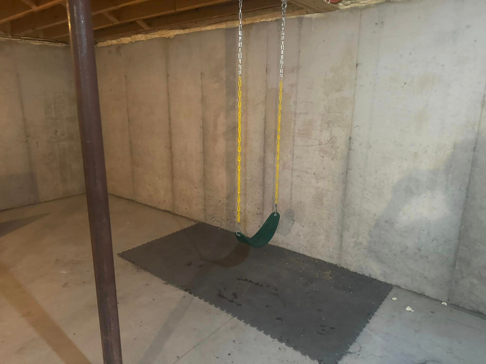 An empty basement with a swing hanging from the ceiling