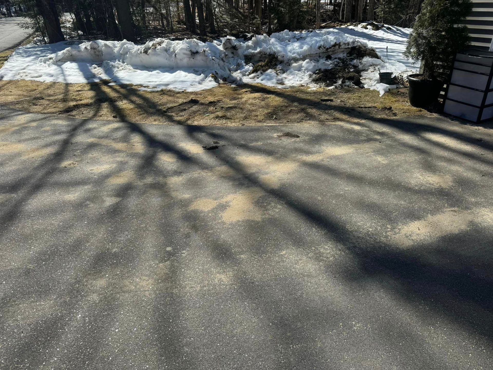 A driveway with snow on the ground and shadows of trees on it.