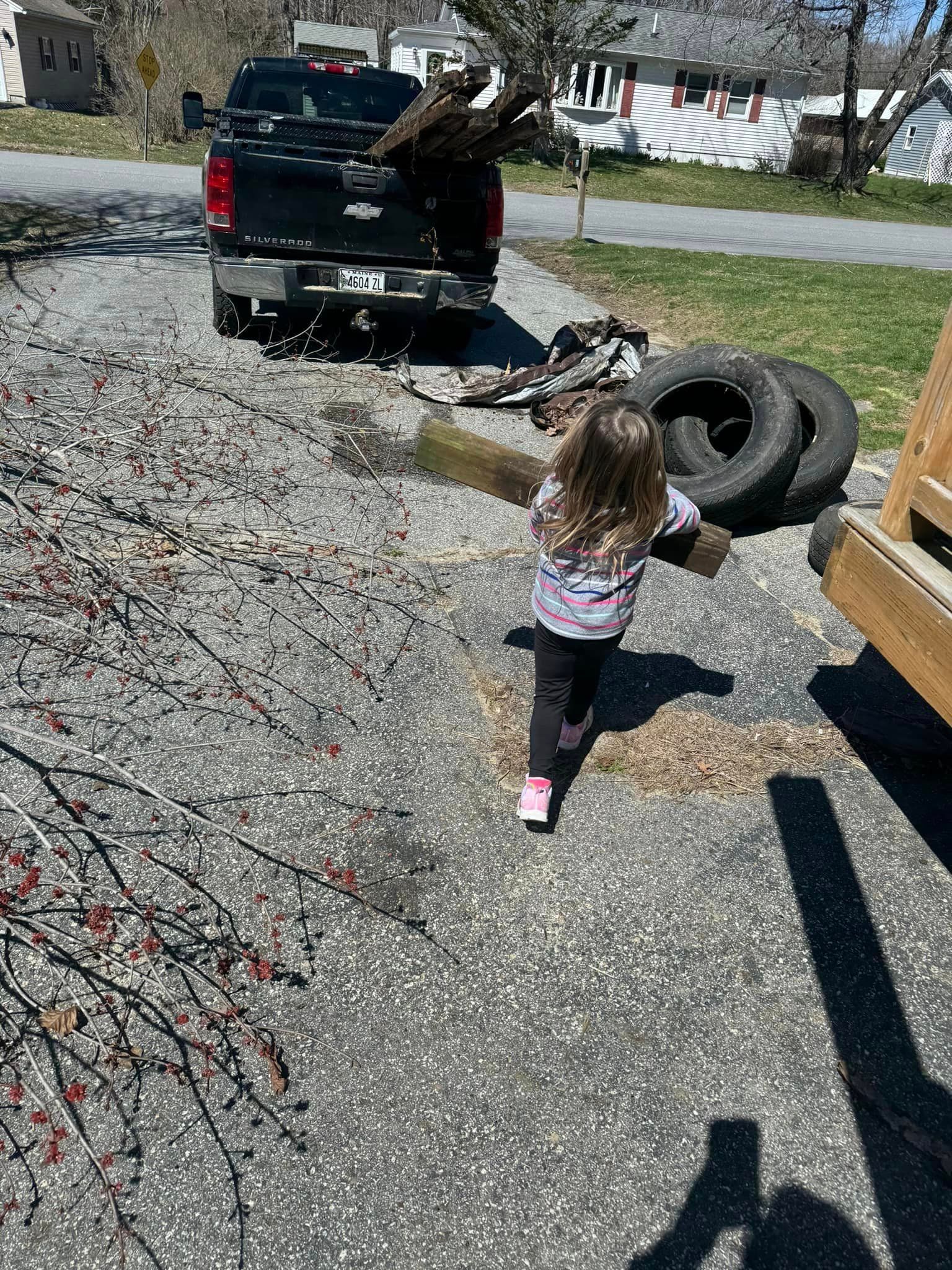 A little girl is running towards a truck carrying a large log.