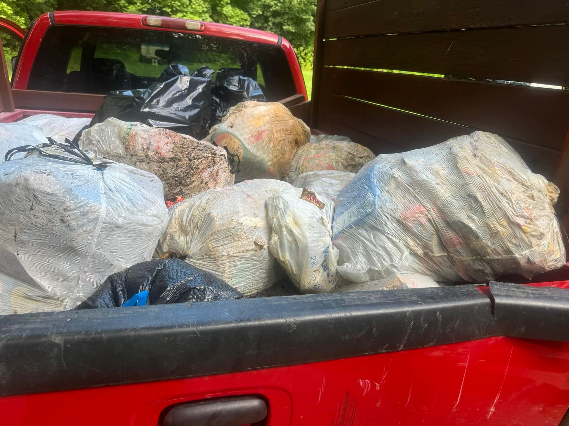 The back of a red truck is filled with bags of rocks.