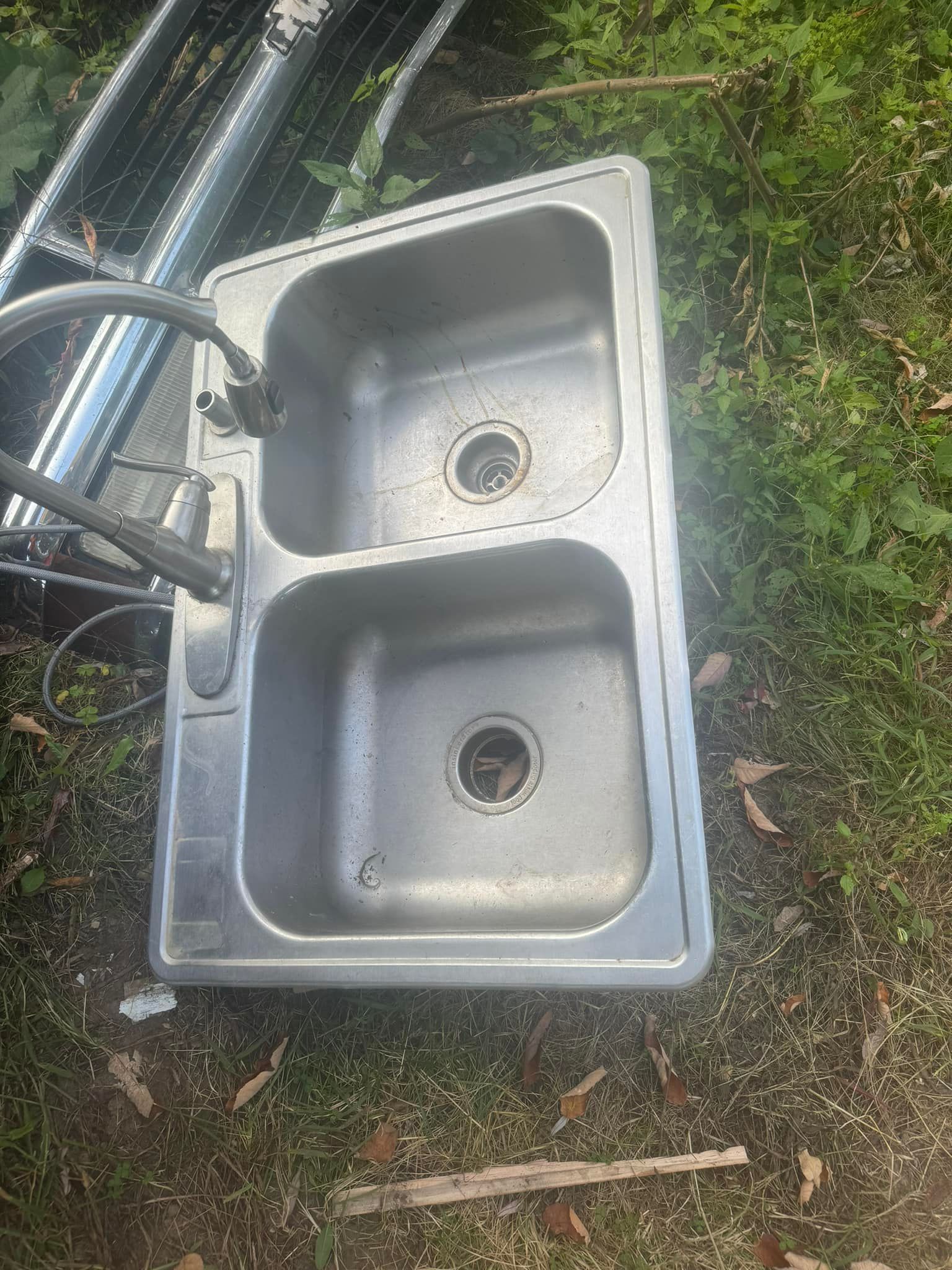 A stainless steel kitchen sink is sitting on top of a lush green field.