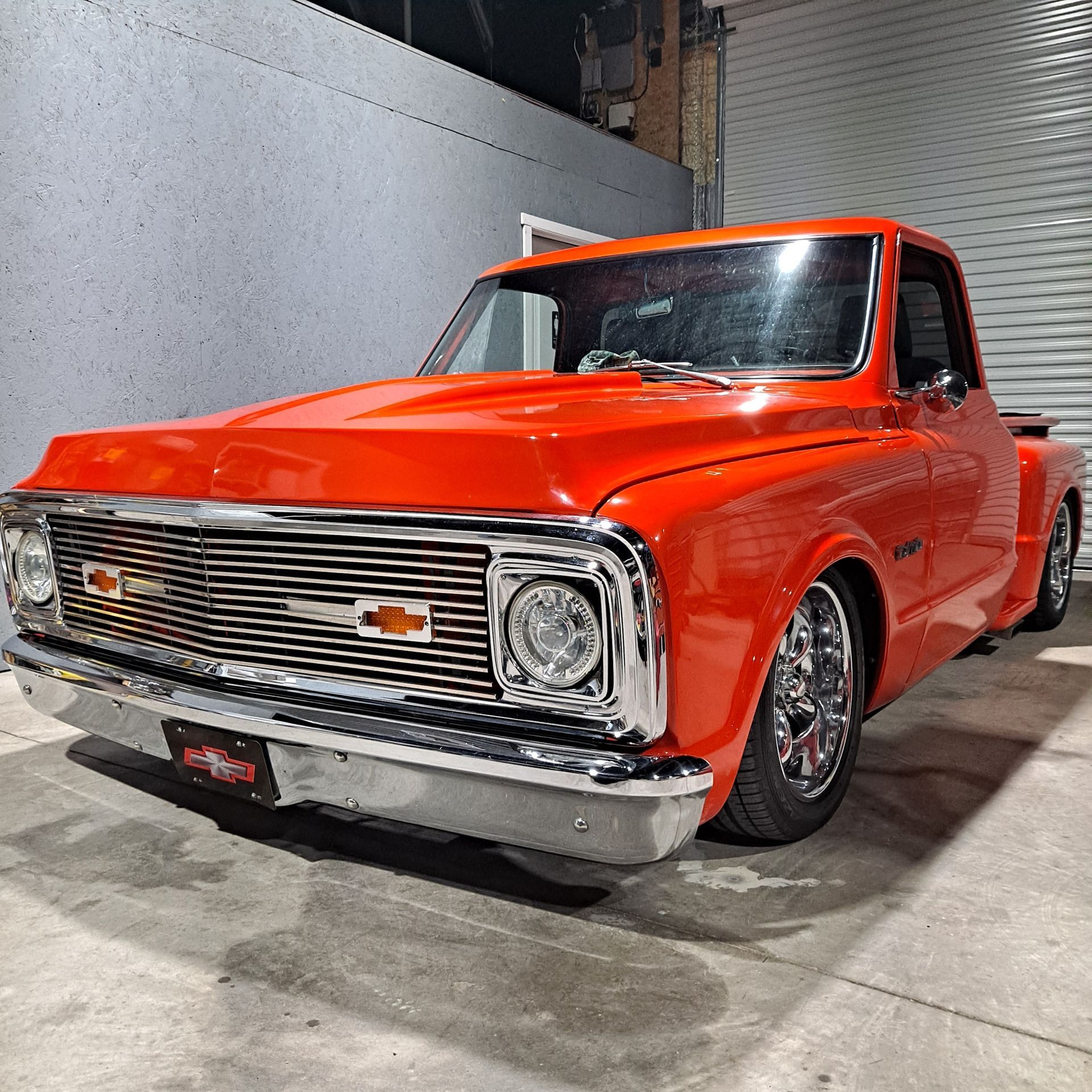 Bright orange classic Chevy C10 pickup truck parked in a garage, chrome detailing.