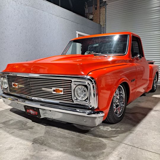 Bright orange classic Chevy C10 pickup truck parked in a garage, chrome detailing.