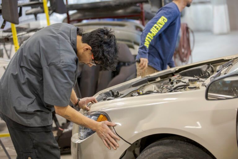 Mechanic inspecting car in a garage. Another person in background.