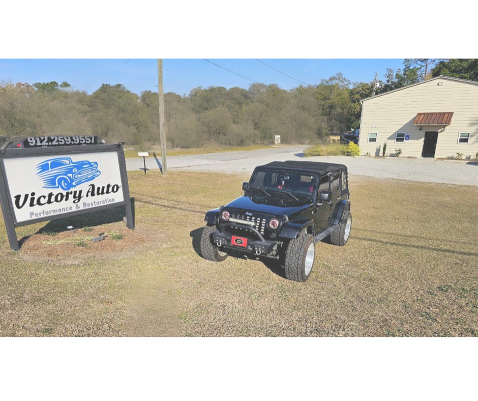 A person welds on a car's rear body panel, wearing a welding helmet and protective clothing, in a garage.