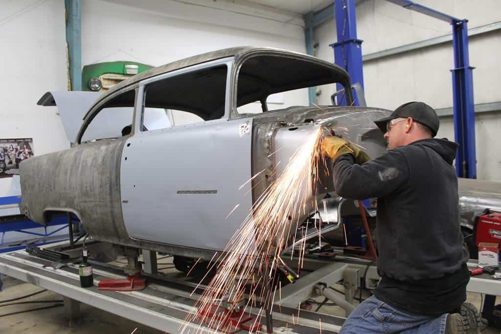 Man in workshop using a grinder on a classic car body, sparks flying.