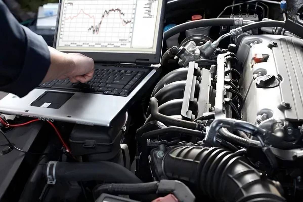 Mechanic uses a laptop to diagnose a car engine. The computer displays data with red and white lines.