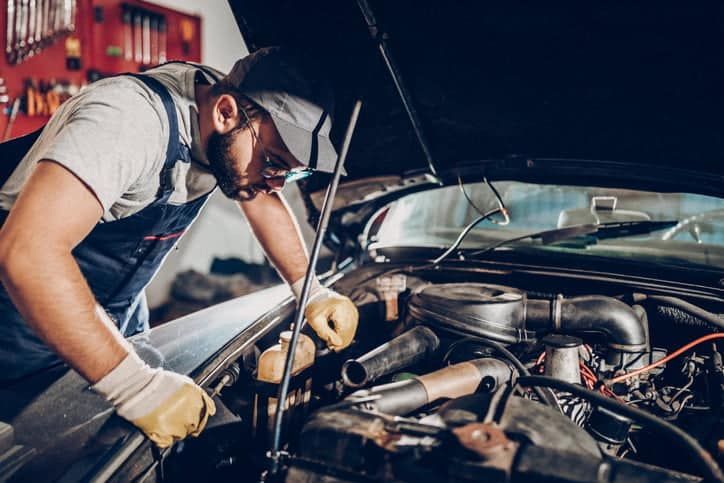 Mechanic in overalls and gloves working on a car engine in a garage.